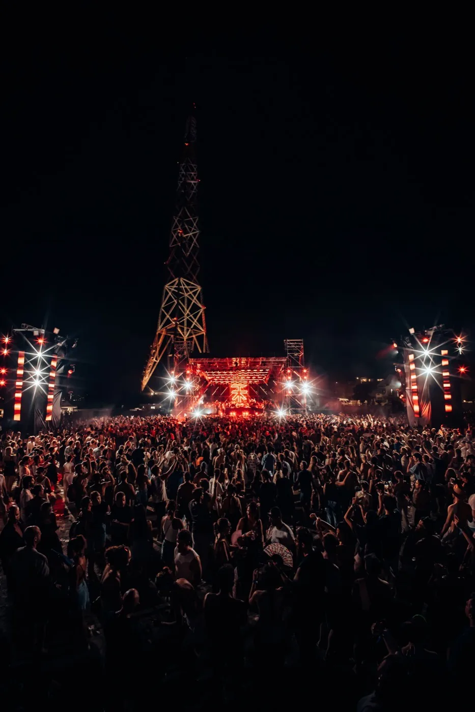 The Atarashi Goes to Sicily stage lit red beneath the Torre Faro pylon, with the crowd in the foreground